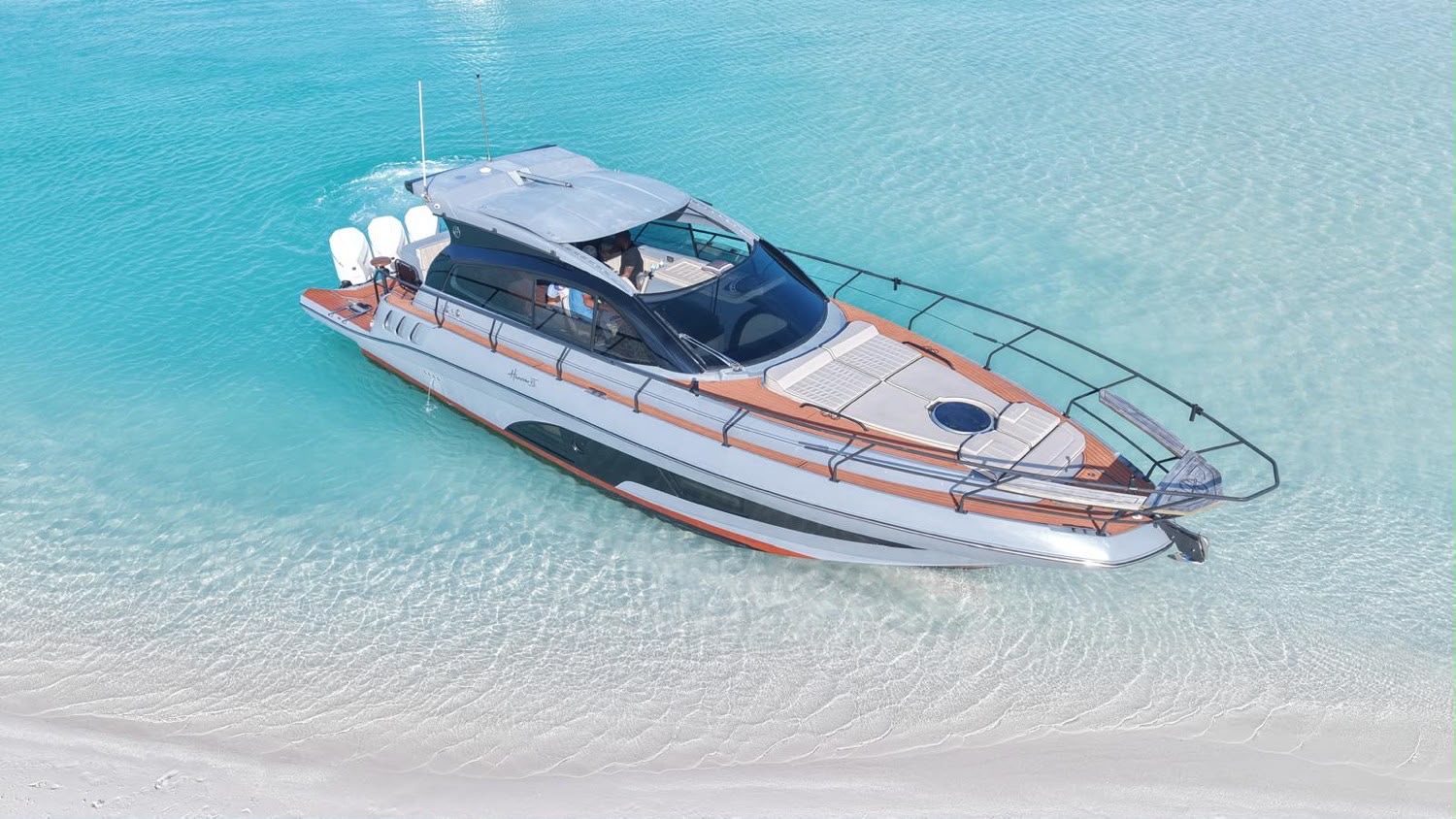 Grey and brown motor yacht anchored in clear turquoise shallows by the beach